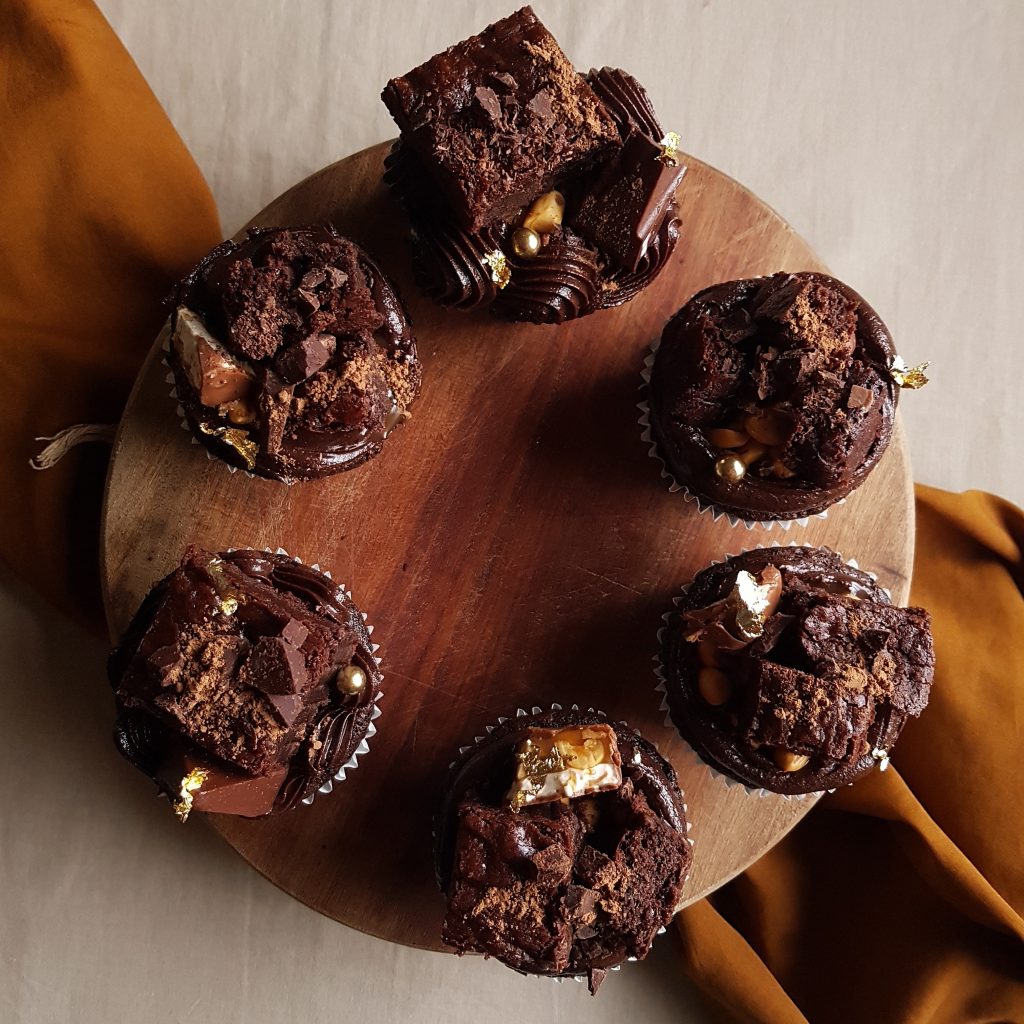 Double chocolate cupcakes with double chocolate buttercream and double chocolate brownie, snickers, caramel sauce, toblerone, peanuts, crushed dark chocolate and gold leaf 